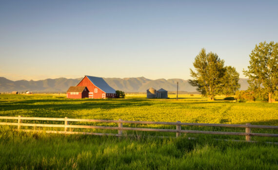 Summer sunset with a red barn and silos in rural Montana with Rocky Mountains in the background.